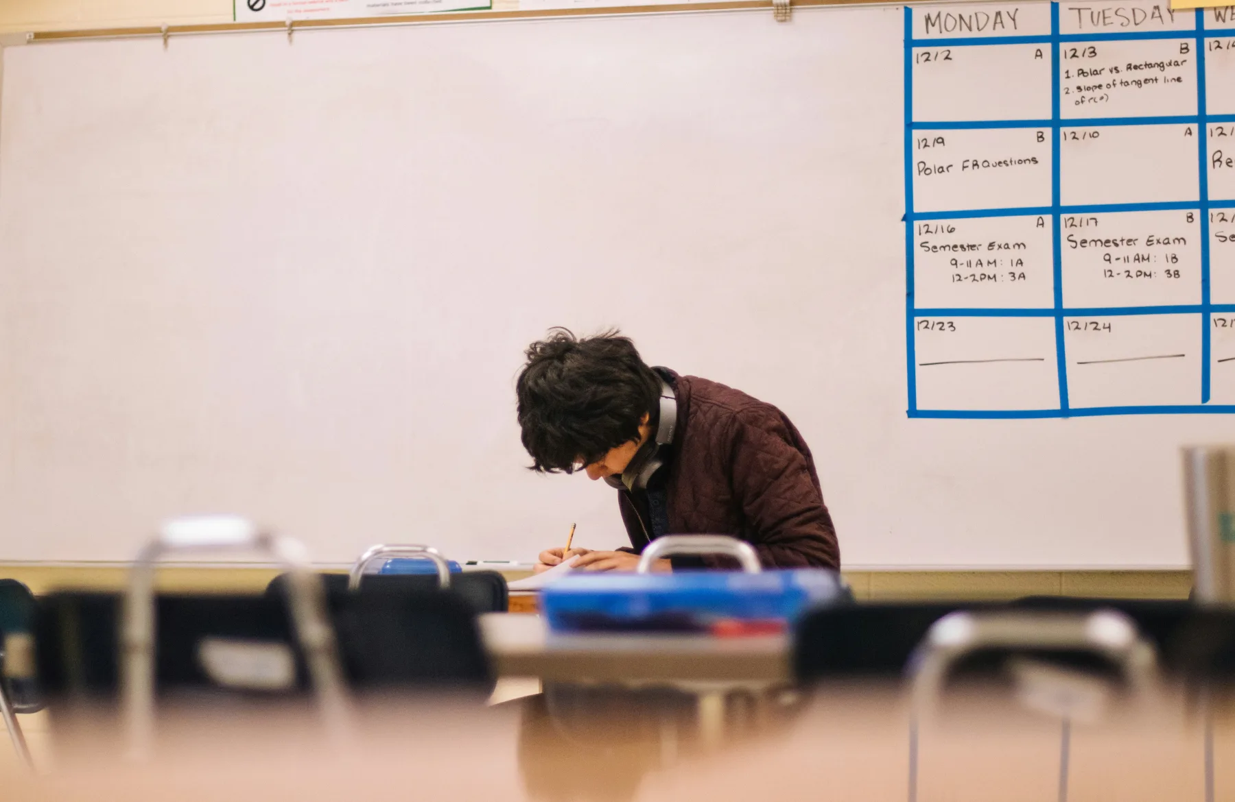 A student writing at a classroom desk.