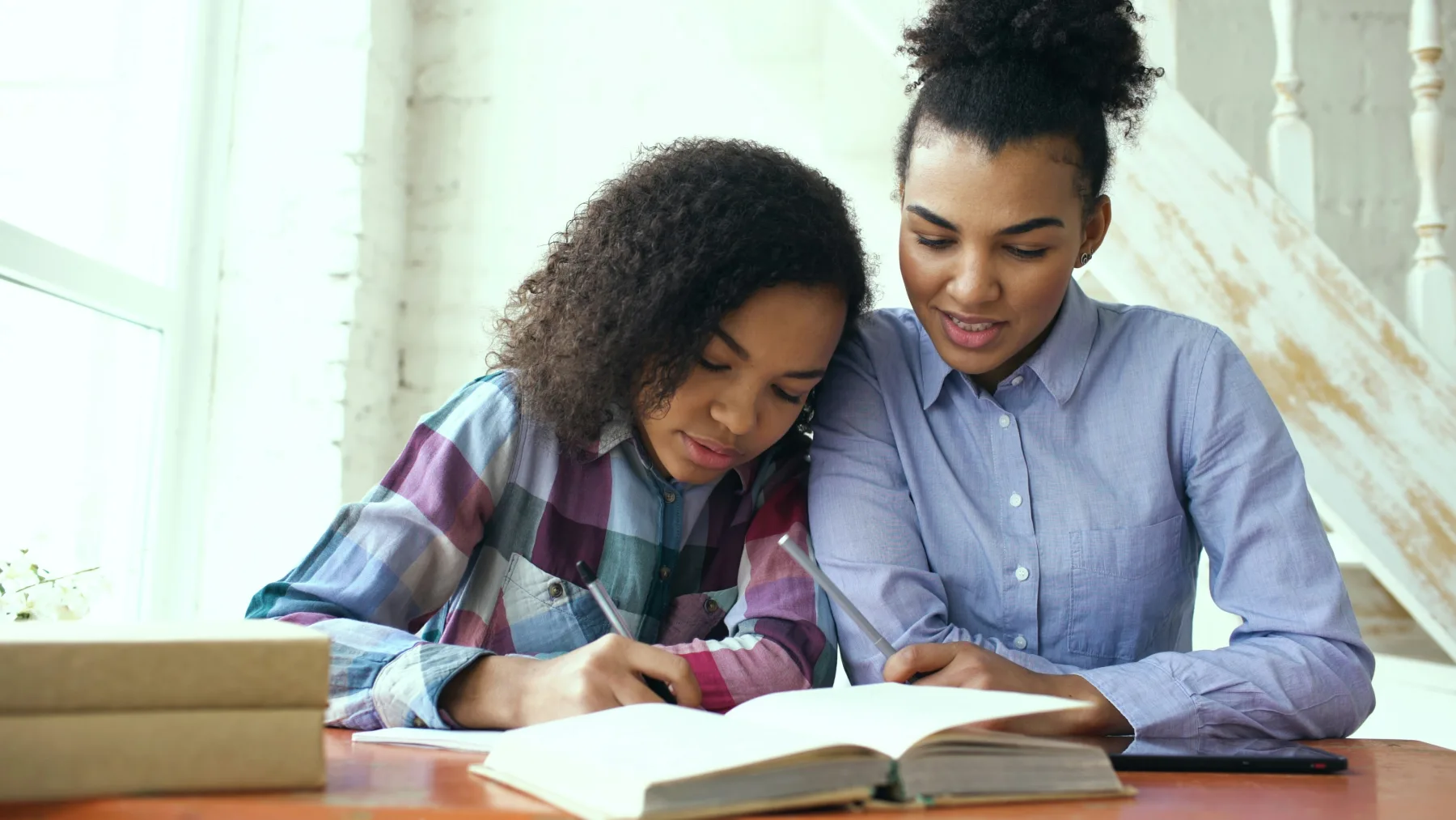 A mentor helping a student write in a workbook beside a laptop.