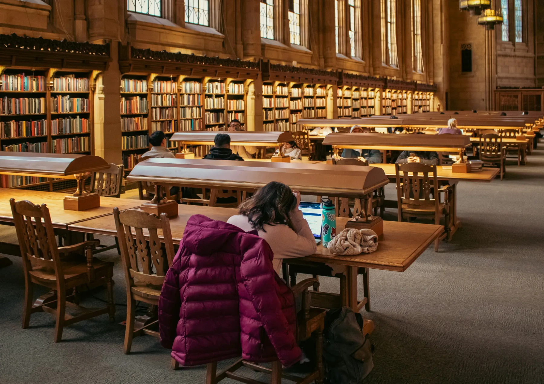 Students gathered around a library table with books and a laptop.